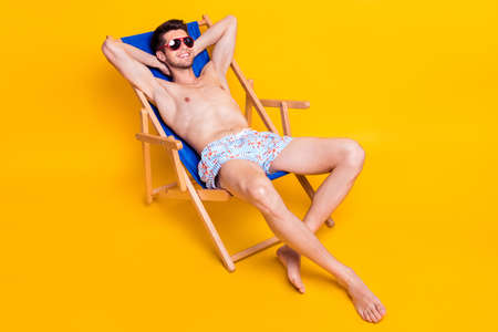 Photo of pretty adorable man naked torso wear dark glasses lying deck chair arms behind head smiling...