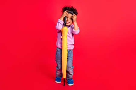 Full length body size view of attractive cheerful funny kid holding parasol hiding isolated over bright red color backgroundの写真素材