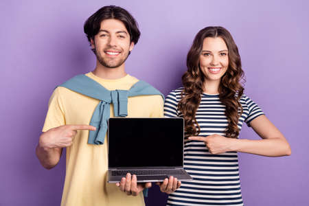 Photo of excited sweet couple wear casual clothes smiling pointing finger modern gadget empty space isolated violet color backgroundの写真素材