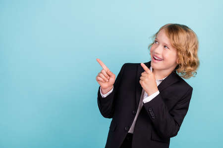 Photo of funny small blond boy point empty space wear uniform isolated on blue color backgroundの写真素材