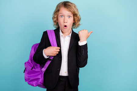 Photo of impressed little blond boy point empty space wear bag uniform isolated on blue color...