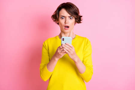 Photo of young shocked amazed surprised girl blogger influencer see dislike in phone isolated on yellow color backgroundの写真素材