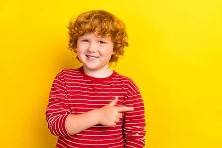 Photo of funky small boy point empty space wear red shirt isolated on yellow color backgroundの写真素材