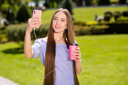 Portrait of attractive cheerful girl strolling traveling using device blogging drinking latte green...