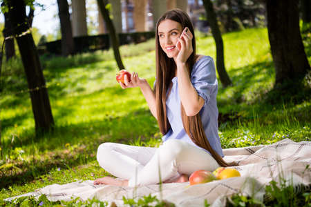 Portrait of attractive trendy cheerful girl sitting on plaid talking on phone discussing news at downtown outdoorsの写真素材