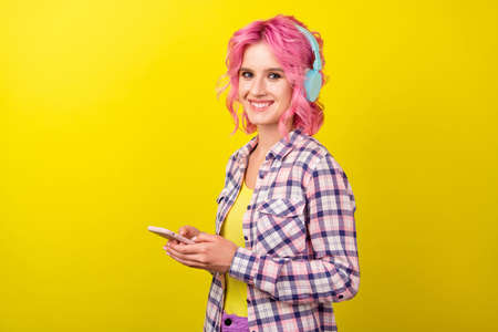 Profile photo of funny pink hairdo young lady hear music hold telephone wear plaid shirt isolated on yellow color backgroundの写真素材