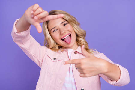 Portrait of positive carefree teen tongue out arms make frame symbol isolated on violet color...