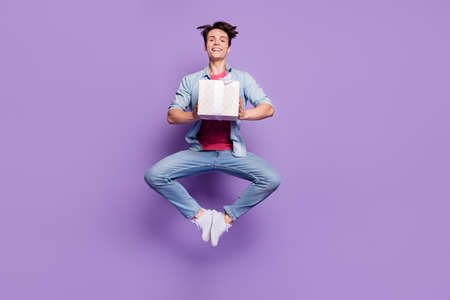 Full size photo of young guy happy positive smile guest hold present box fly air jump isolated over purple color backgroundの写真素材