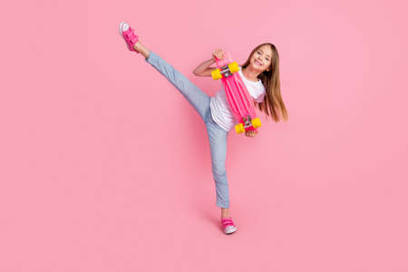 Full body photo of sweet blond small girl hold skate wear white t-shirt jeans isolated on pink color backgroundの写真素材