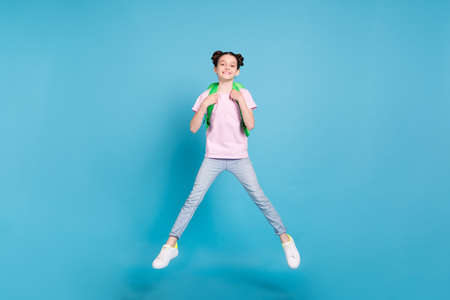 Photo of charming cute schoolgirl dressed pink t-shirt rucksack jumping high smiling isolated blue color backgroundの写真素材
