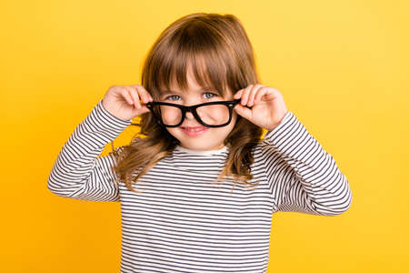 Photo of friendly little blond hair girl touch spectacles wear striped shirt isolated on yellow color backgoundの写真素材