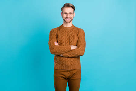 Photo of charming cute young gentleman wear brown pullover glasses arms crossed smiling isolated blue color backgroundの写真素材