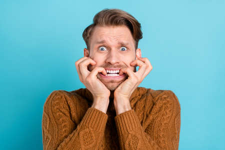 Photo of pretty scared young gentleman wear brown pullover biting fingers isolated blue color backgroundの写真素材