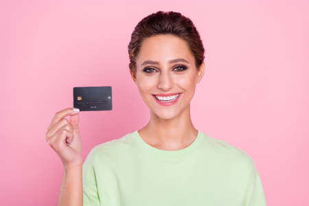 Photo of positive happy nice young woman hold hands credit card smile money isolated on pink color...