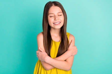 Photo of optimistic nice brown hair girl hug herself wear yellow dress isolated on bright teal color backgroundの写真素材