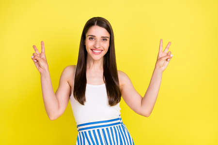 Portrait of attractive cheerful girl showing double v-sign having fun isolated over bright yellow...