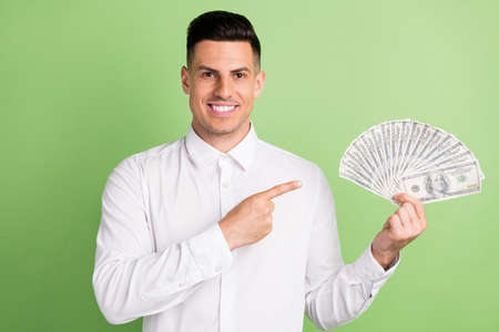 Photo of charming cute young gentleman wear white shirt smiling pointing finger cash fan isolated green color backgroundの写真素材