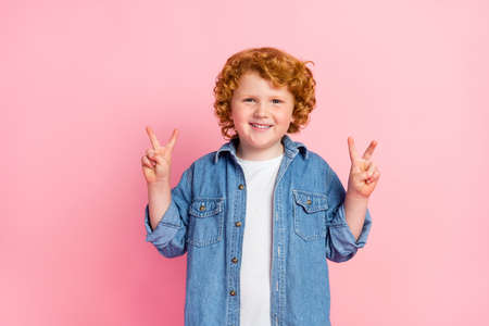 Photo of nice adorable little boy show two v-signs beaming smile wear denim jacket isolated pink...
