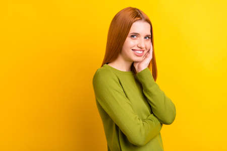Photo portrait red haired woman in green sweater smiling touching cheek isolated vivid yellow color...