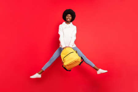 Full length photo of funny brunette millennial lady jump with bag wear hoodie jeans isolated on red backgroundの写真素材