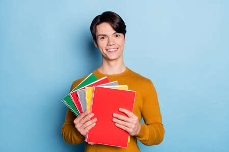 Photo of good brunet young guy hold books wear brown sweater isolated on blue color backgroundの写真素材