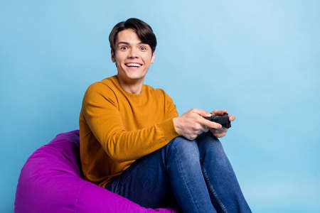 Photo of funky brunet millennial guy sit on bag wear sweater jeans isolated on blue color background