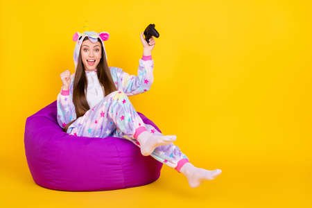 Portrait of attractive cheerful girl sitting in chair having fun playing game isolated over bright yellow color backgroundの写真素材