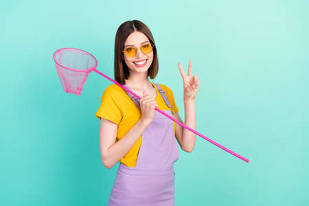 Photo of pretty young positive woman make v-sign hold net wear sunglass summer isolated on teal...
