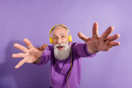 Portrait of attractive cheerful grey-haired man listening music touching you having fun isolated...