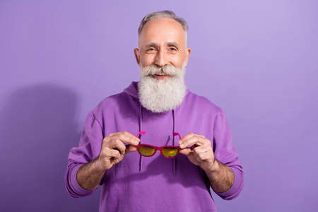 Portrait of attractive cheerful grey-haired man holding specs wearing season clothes isolated over...