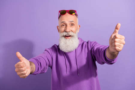Portrait of attractive elderly cheerful grey-haired man showing double thumbup solution isolated over purple violet color backgroundの写真素材