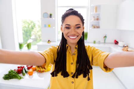 Photo of pretty funny dark skin lady wear yellow shirt dreadlocks smiling tacking selfie indoors...
