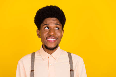 Photo of cheerful dreamy inspired african guy look empty space wear suspenders shirt isolated yellow...