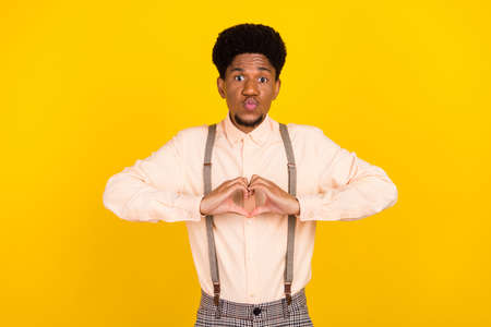 Photo of affectionate guy blow air kiss show heart symbol wear suspenders shirt isolated yellow color backgroundの写真素材