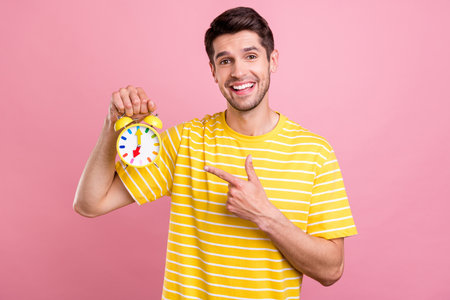Portrait of attractive cheerful guy demonstrating vintage retro clock minute isolated over pink...