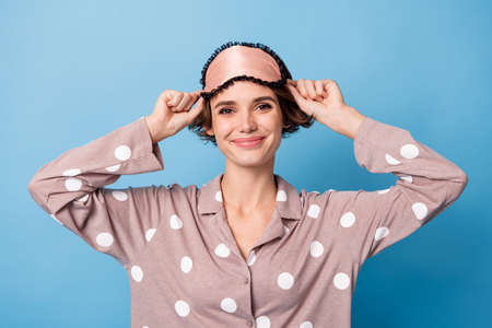 Photo of young beautiful lovely cheerful smiling girl wear eye mask and pajamas isolated on blue color backgroundの写真素材