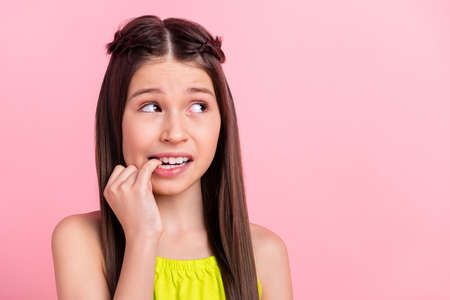 Photo of doubtful unsure small schoolgirl dressed yellow outfit biting finger looking empty space...