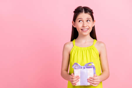 Photo of funny cute school girl wear yellow clothes smiling holding birthday gift looking empty space isolated pink color backgroundの写真素材