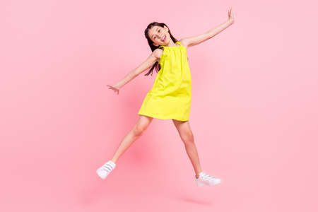 Full length photo of sweet shiny school girl wear yellow dress dark eyewear jumping high isolated pink color backgroundの写真素材