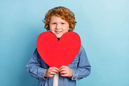 Photo portrait curly little boy smiling showing red heart postcard isolated pastel blue color...
