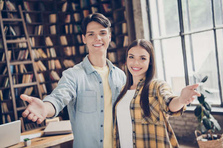 Portrait of two attractive cheerful friends welcoming you to library at loft industrial interior indoorsの写真素材