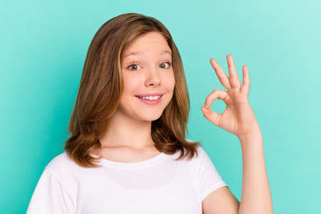 Photo portrait little girl smiling showing okay gesture in white t-shirt isolated bright turquoise...