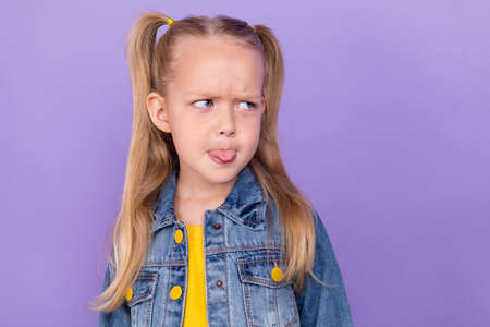 Photo of young small girl unhappy grimace tongue-out conflict offensive rude look empty space isolated over violet color backgroundの写真素材