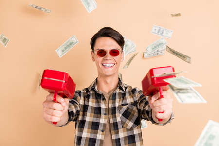 Photo of handsome wealthy guy hold gun throw dollars wear sunglass plaid shirt isolated beige color...
