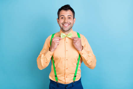 Photo of positive boyfriend guy adjust accessories wear green suspenders shirt bow tie isolated blue color backgroundの写真素材