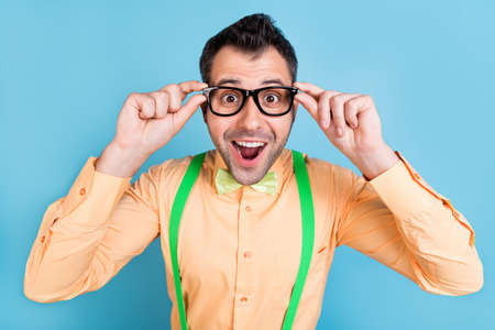 Photo of impressed brunet young man touch eyewear wear peach shirt spectacles isolated on blue color...