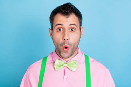 Photo of amazed shocked guy open mouth wear green suspenders pink shirt bow tie isolated blue color backgroundの写真素材