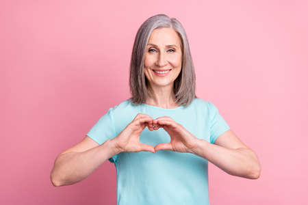 Photo of funny elder grey hairdo lady hand heart wear teal blouse isolated on pink color backgroundの写真素材