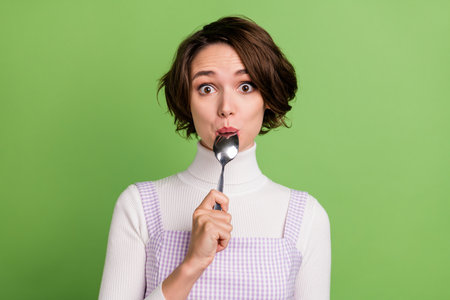 Photo of young girl amazed shocked lick cutlery spoon weight loss dieting isolated over green color backgroundの写真素材