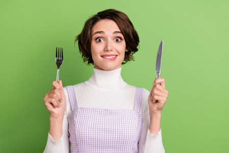 Photo of young girl happy positive smile bite lips teeth hold cutlery fork knife hungry isolated over green color backgroundの写真素材